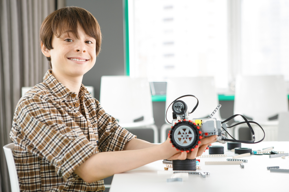 featured image showing Excited young boy smiling to the camera holding a robot he is building