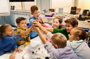 Featured image showing group of happy kids building robots and making high five gesture at robotics school