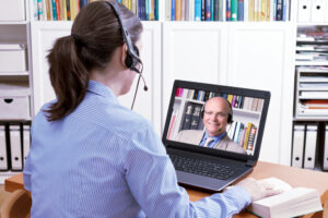 Featured image showing a professional woman with a headset in front of her laptop and doing an online video call with a professionally dressed man. Virtual job interview concept.