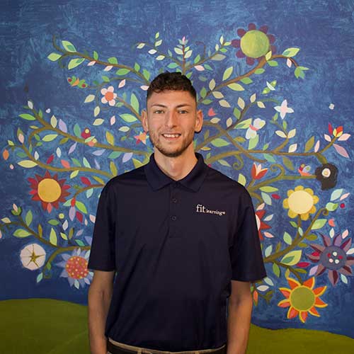 Featured image showing Marcus Spencer, employee at Fit Learning standing in front of a colorful mural of flower onsite at Fit Learning Center.